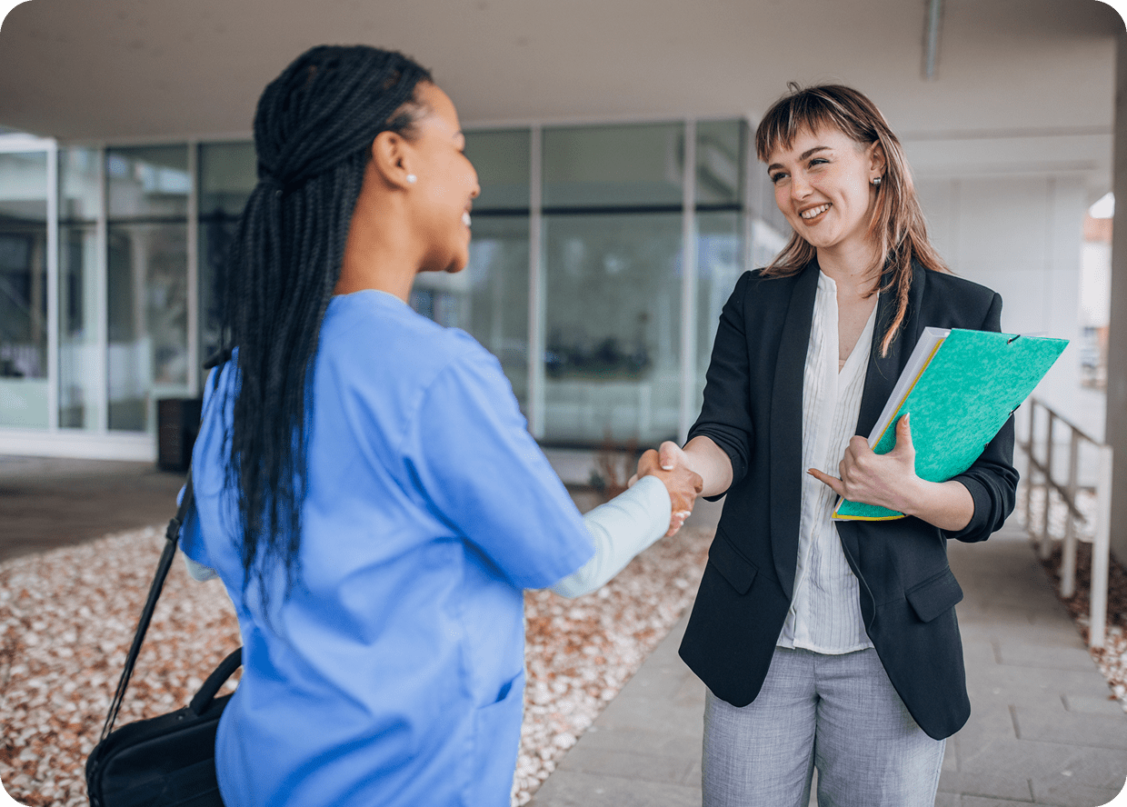 Two women shaking hands outside a building.